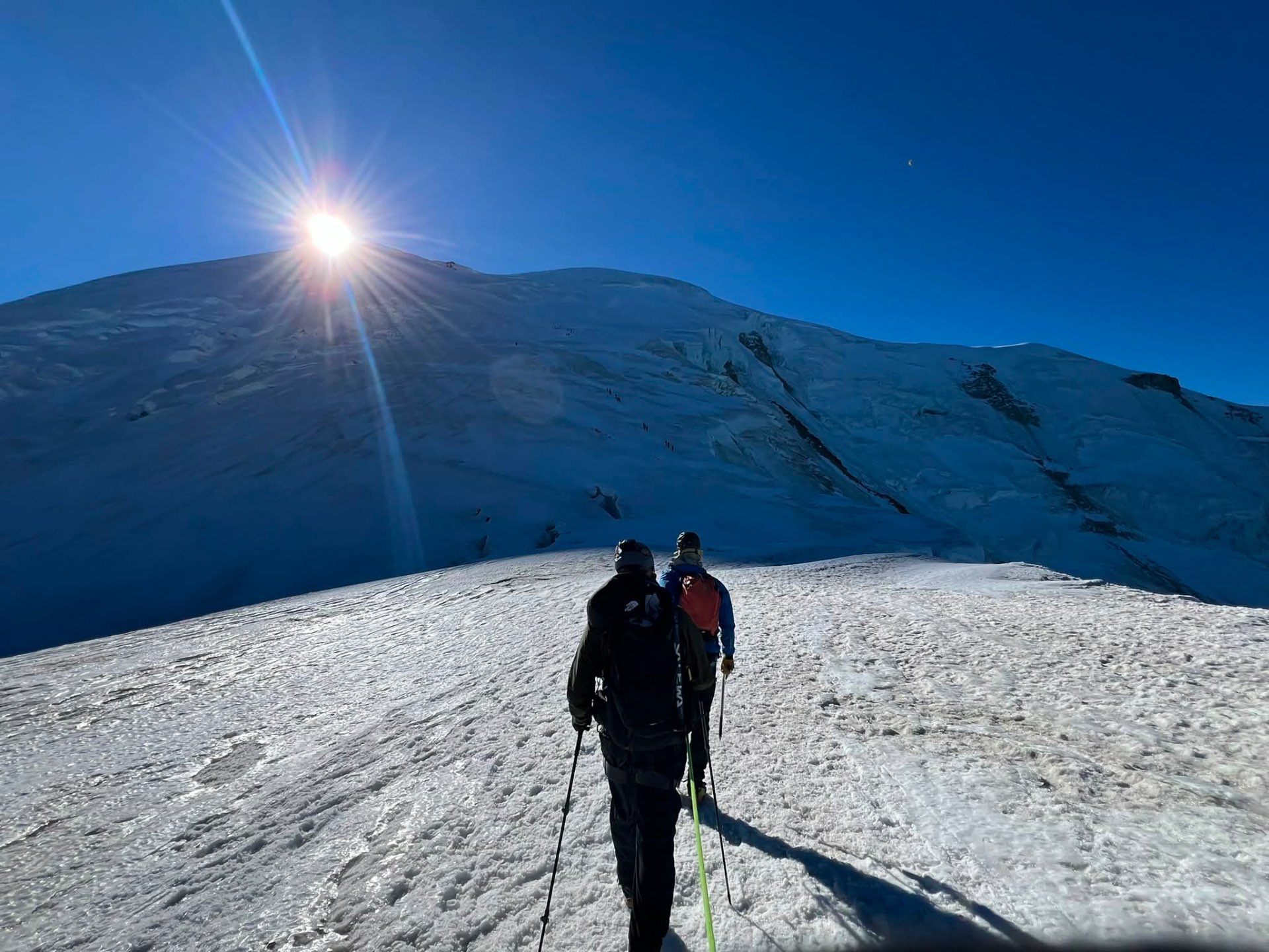 Two climbers walking across a wide glacier under bright sun.